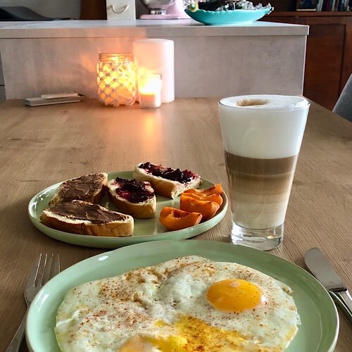 Frühstück Spiegeleier, Latte Macchiato, Stuten, Marille, Kerzen im Hintergrund